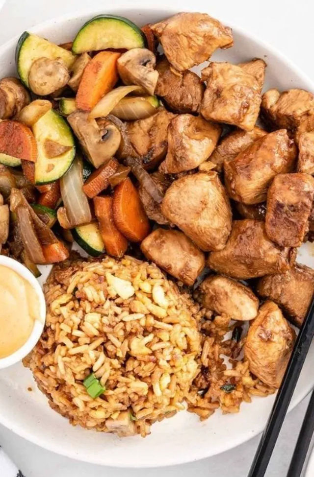 Savory teriyaki chicken bowl with cubed glazed chicken, zucchini-carrot-mushroom stir-fry, seasoned fried rice, dipping sauce and chopsticks