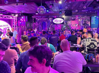 Lively purple-lit Dallas bar interior with disco balls, mirrored tile wall and a crowded room of patrons seated at high tables enjoying drinks and live music