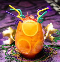 Festive Mardi Gras cocktail in a glass with orange slices and cherries over crushed ice, topped with colorful curly straws and surrounded by purple, green and gold beads and decorative masks on a purple backdrop.