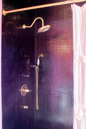 Black mosaic-tile shower with gold rain showerhead, gold handheld and fixtures, and a pink ruffled shower curtain — modern bathroom detail