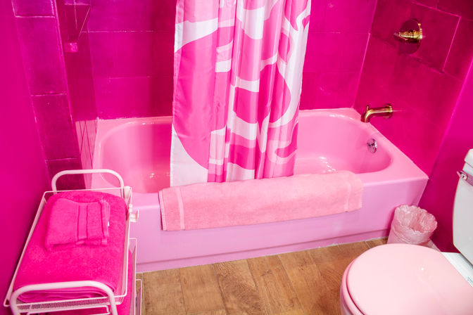 Playful retro all-pink bathroom with a pink bathtub and patterned shower curtain, matching towels, pink toilet, and wood-look flooring.