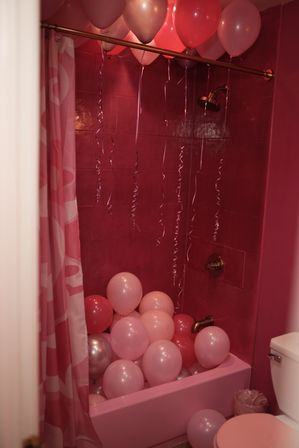 Pink tiled bathroom with shower and bathtub filled with pink and rose-gold party balloons and hanging ribbon streamers
