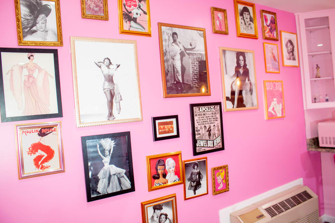 Bright pink room interior with a playful gallery wall of framed vintage pin‑up photos, retro posters and glamour portraits arranged above a wall heater.
