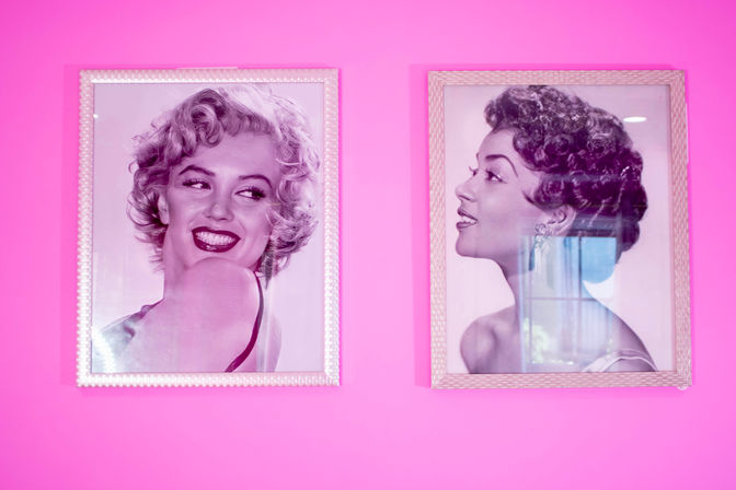 Two framed black-and-white vintage glamour portraits of smiling women on a bright pink wall — one looking over her shoulder and laughing, the other shown in profile with glass reflections adding sparkle.