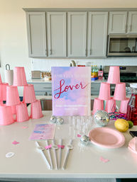 Pink-themed bachelorette weekend setup on a modern kitchen island with stacked pink plastic cups, pastel sign referencing Austin, Texas, mini disco balls, clear shot glasses, pink plates and party straws.