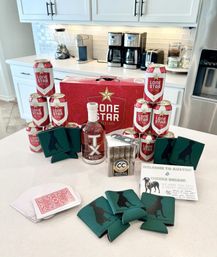 Austin, Texas party welcome display on a kitchen island with Lone Star beer cans and case, TX whiskey bottle, box of cigars, green dog-silhouette koozies, playing cards and a guest welcome note.