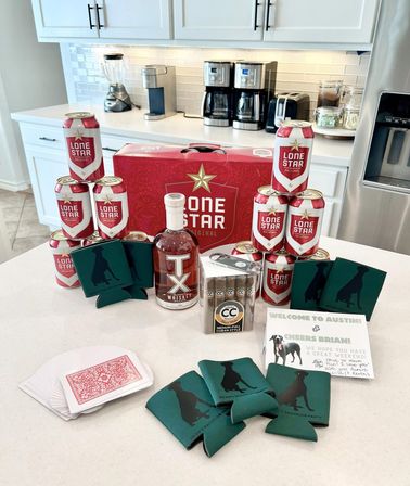 Austin, Texas party welcome display on a kitchen island with Lone Star beer cans and case, TX whiskey bottle, box of cigars, green dog-silhouette koozies, playing cards and a guest welcome note.