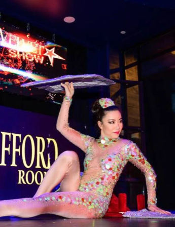 Cabaret acrobat in a sparkling sequin bodysuit striking a flexible pose on stage, balancing a flat board on one hand under colorful spotlights