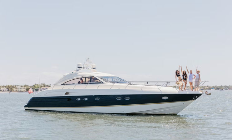 Luxury white-and-navy motor yacht cruising calm coastal waters with a group of people cheering on the bow under a clear sky and an American flag at the stern