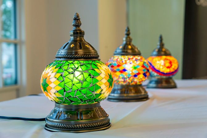 Row of colorful Turkish mosaic glass table lamps on a white table; close-up of a green geometric lamp with ornate brass base and warm glow.