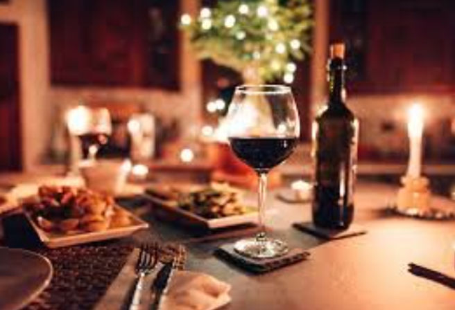 Romantic candlelit dinner setting with a glass of red wine, wine bottle, plates of food, and twinkling lights.