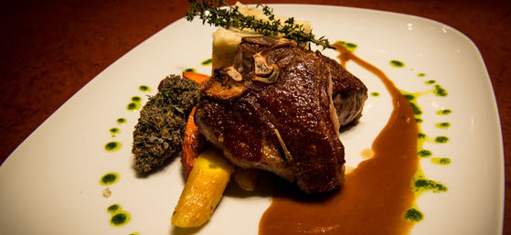 Gourmet seared bone-in steak with brown jus, roasted root vegetables, mashed potato, herb oil dots and thyme sprig on a white plate in a fine-dining presentation.