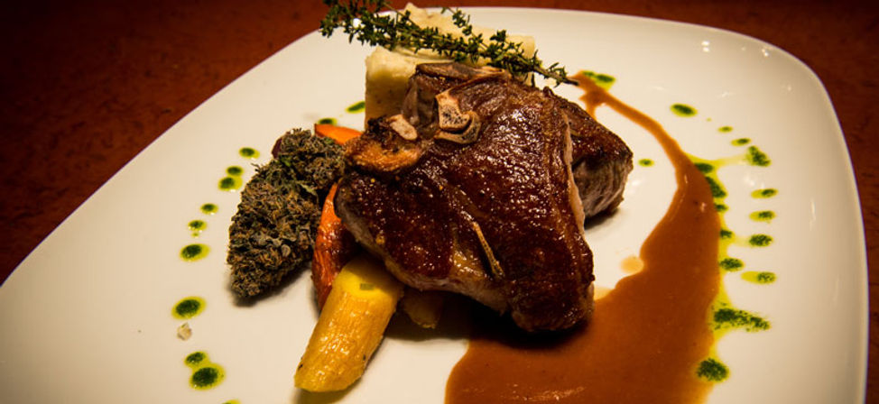 Gourmet seared bone-in steak with brown jus, roasted root vegetables, mashed potato, herb oil dots and thyme sprig on a white plate in a fine-dining presentation.