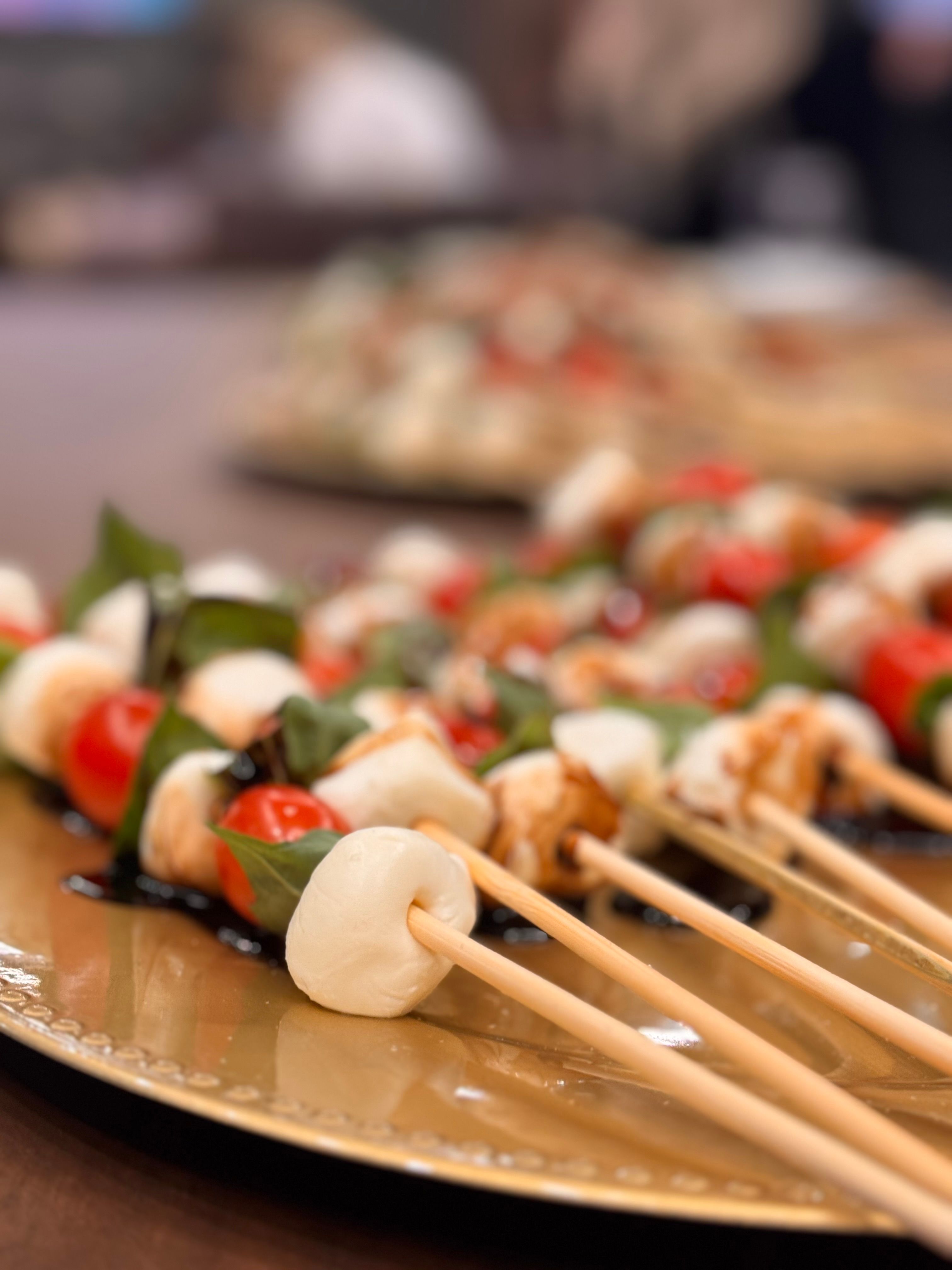 Close-up of Italian-inspired Caprese appetizer skewers with fresh mozzarella, cherry tomatoes and basil drizzled with balsamic glaze on a gold serving platter