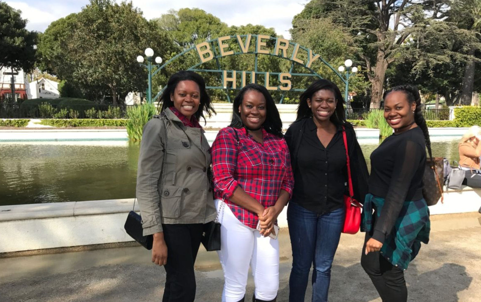 Four smiling women posing in front of the iconic Beverly Hills sign and reflecting pond in Los Angeles