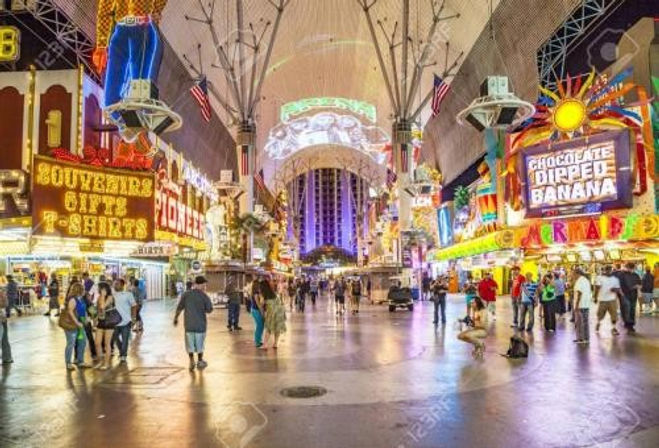 Night scene on Fremont Street Experience in downtown Las Vegas — neon signs, LED canopy projections, souvenir shops and snack stands lining a busy pedestrian mall with people strolling.