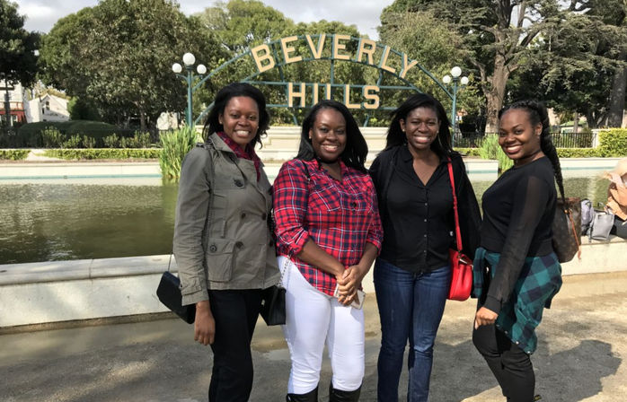 Four smiling women posing in front of the Beverly Hills sign and reflecting pond in Los Angeles