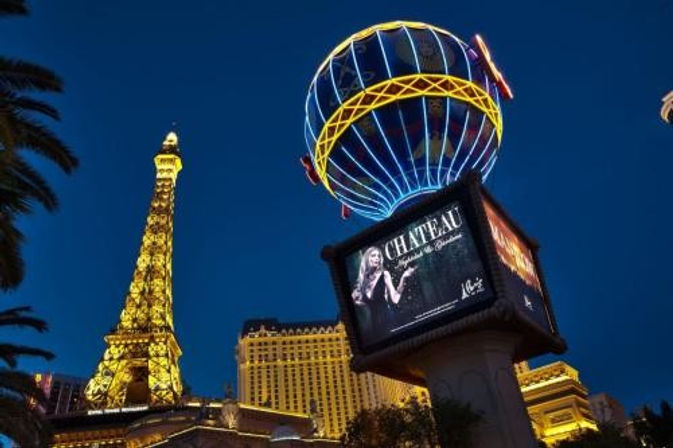 Neon-lit Eiffel Tower replica beside a glowing hot-air-balloon billboard above casino buildings on the Las Vegas Strip at night