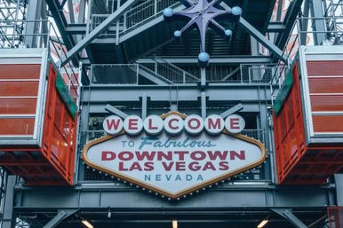 Retro marquee sign reading "Welcome to Fabulous Downtown Las Vegas Nevada" hung in an industrial steel canopy with a purple starburst accent and orange gondola pods