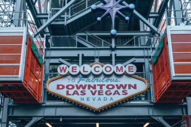 Retro marquee sign reading "Welcome to Fabulous Downtown Las Vegas Nevada" hung in an industrial steel canopy with a purple starburst accent and orange gondola pods