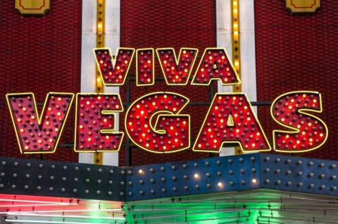 Vibrant vintage neon marquee reading "VIVA VEGAS" in red bulb letters outlined in yellow over a blue and green lit canopy — classic Las Vegas sign.