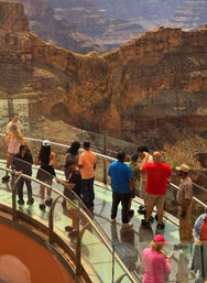 Visitors on a curved glass skywalk above a vast orange-brown desert canyon with dramatic layered cliffs — Arizona scenic overlook