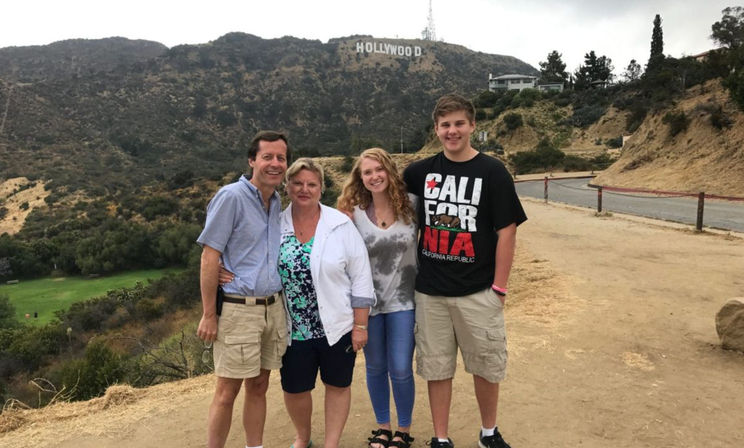 Group of four smiling people posing on a dirt overlook with the Hollywood Sign on the hillside in the Hollywood Hills, Los Angeles