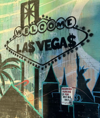 Playful Las Vegas street-art mural of a dripping "Welcome to Las Vega$" sign painted on a textured wall, featuring palm trees, stylized skyline and a Statue of Liberty silhouette — vibrant urban graffiti in Nevada.