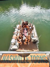 Aerial view of friends in swimsuits partying with red-cup drinking game on a pontoon boat on a green Nashville-area lake.