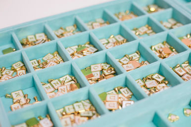 Turquoise compartment tray filled with gold‑edged pastel alphabet letter charms, neatly sorted craft jewelry supplies.