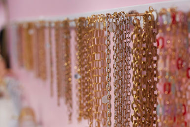 Close-up of shimmering gold chain necklaces hanging on a white rack against a pink wall, boutique jewelry display