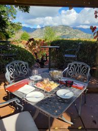Sunlit outdoor patio set for charcuterie and wine, overlooking a vineyard with autumn foliage and rolling hills and mountains under a blue sky