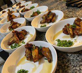 Glazed chicken wings garnished with cilantro in white bowls lined up on a granite countertop, plated for service in a kitchen