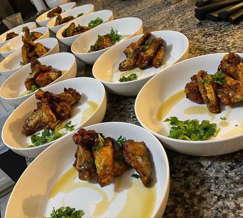 Glazed chicken wings garnished with cilantro in white bowls lined up on a granite countertop, plated for service in a kitchen