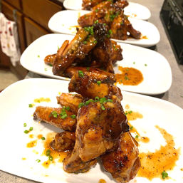 Sticky glazed chicken wings stacked on white plates, drizzled with savory sauce and sprinkled with chopped chives — restaurant-style appetizer
