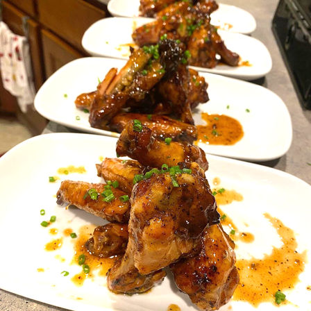 Sticky glazed chicken wings stacked on white plates, drizzled with savory sauce and sprinkled with chopped chives — restaurant-style appetizer