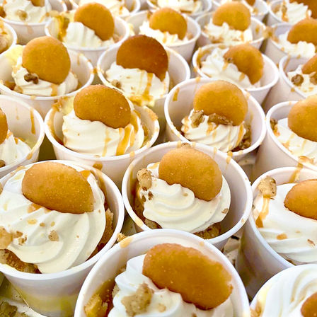 Close-up of rows of bite-sized dessert cups filled with swirled vanilla cream, each topped with a round golden cookie, caramel drizzle and chopped nuts.