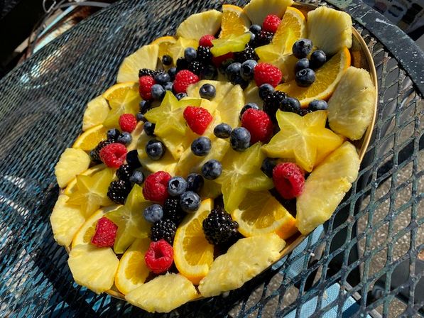Vibrant summer fruit platter with pineapple slices, starfruit, orange wedges, raspberries, blueberries and blackberries on a metal patio table