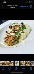 Close-up of two golden pan-seared crab cakes on a bed of creamy grits, drizzled with lemon aioli and garnished with microgreens on a white plate