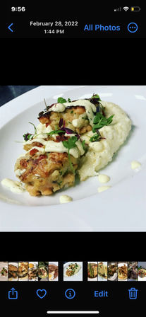 Close-up of two golden pan-seared crab cakes on a bed of creamy grits, drizzled with lemon aioli and garnished with microgreens on a white plate