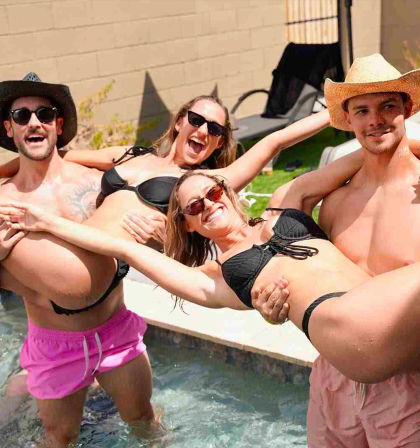 Four friends laughing at a backyard pool party as two men in hats lift two women in black bikinis over the water on a sunny day, sunglasses and fun vibes.