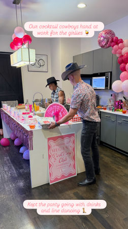 Two bartenders in cowboy hats mixing cocktails at a pink-themed bachelorette-style party in a modern kitchen with balloons and streamers.