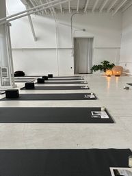 Minimalist white loft yoga studio with rows of black mats and blocks, candles and warm lanterns by a potted plant set for a calm yoga or meditation class