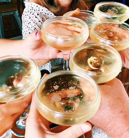 Group clinking champagne coupes in a sparkling toast — bubbly celebration at a brunch or cocktail bar.