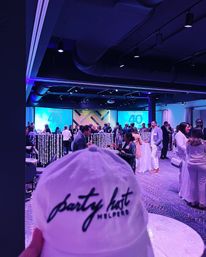 White cap in foreground with script logo, lively purple-lit ballroom networking reception and large "40 Under 40" award screens on stage