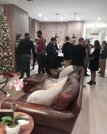 Festive holiday cocktail party in a modern open-concept condo kitchen and living room, guests mingling by the island, decorated Christmas tree and leather sofa