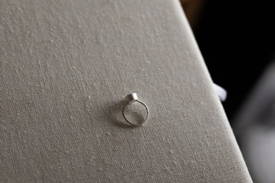 Close-up of a minimalist silver ring with a small cylindrical top resting on beige linen fabric