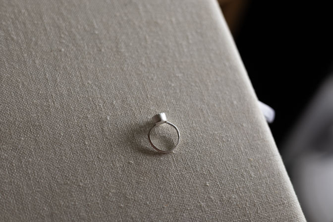Close-up of a minimalist silver ring with a small cylindrical top resting on beige linen fabric