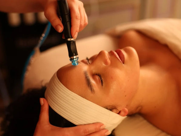 Relaxed client receiving hydrafacial microdermabrasion on forehead with blue-tipped wand during a spa facial treatment