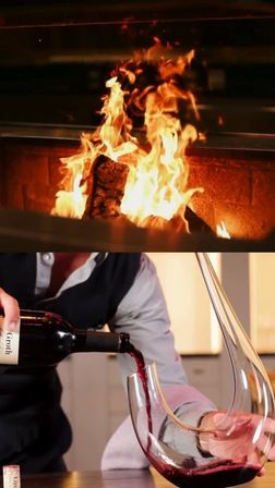 Roaring fireplace above a close-up of red wine being poured into an elegant curved glass decanter, evoking a cozy, warm home dining atmosphere.